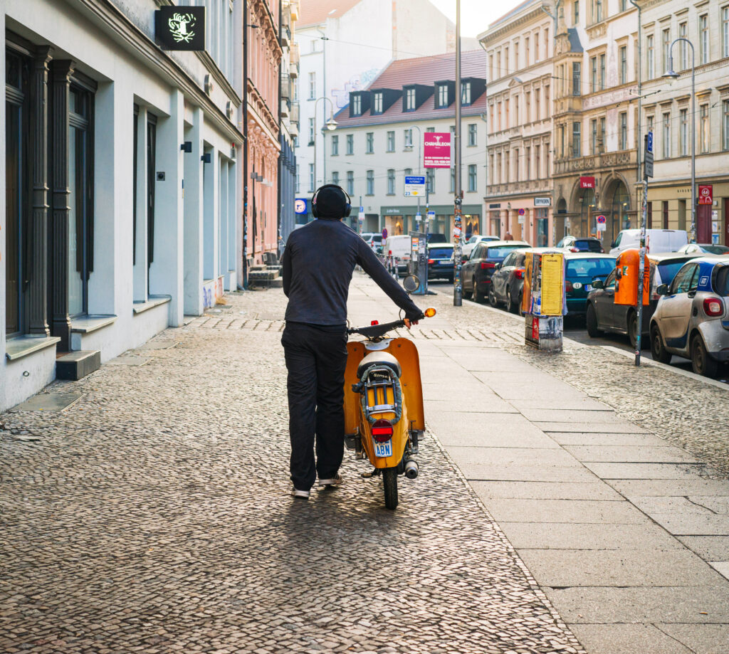 Man from behind pushes his scooter through an old town street in Berlin's Scheunenviertel district